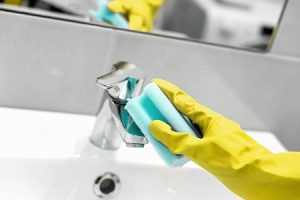 A residential cleaner wiping down a bathroom sink with Kiwi Clean Home